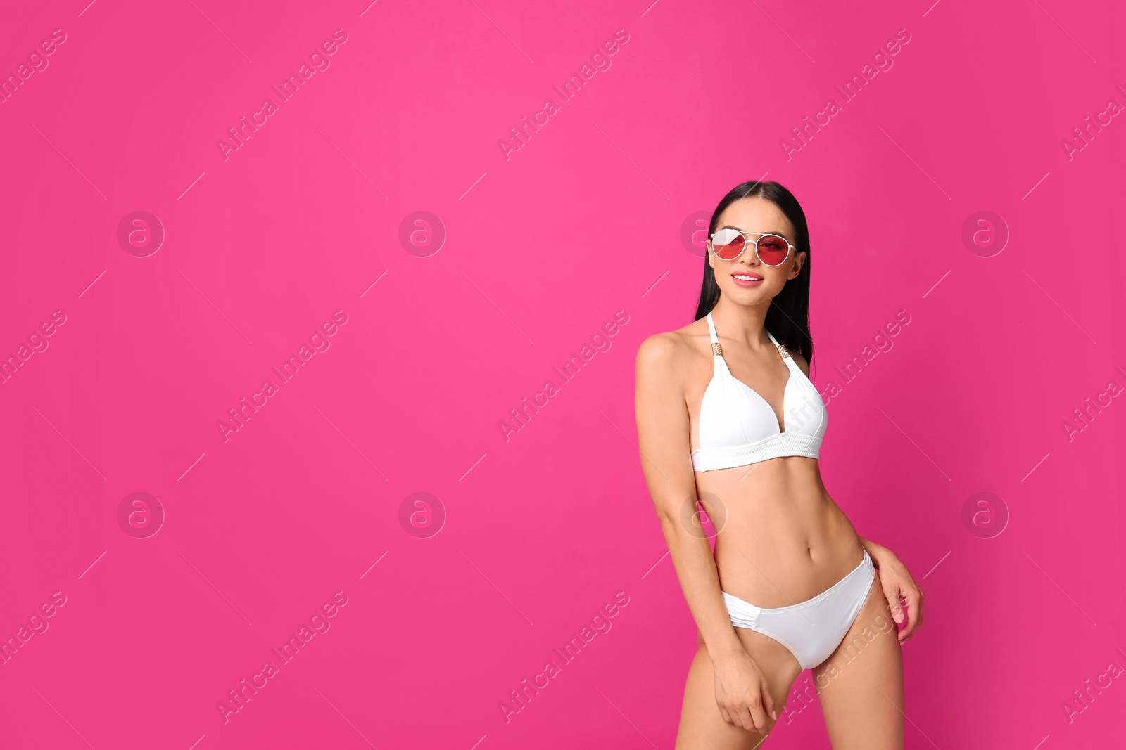 Photo of Beautiful young woman in white bikini with sunglasses on pink background. Space for text