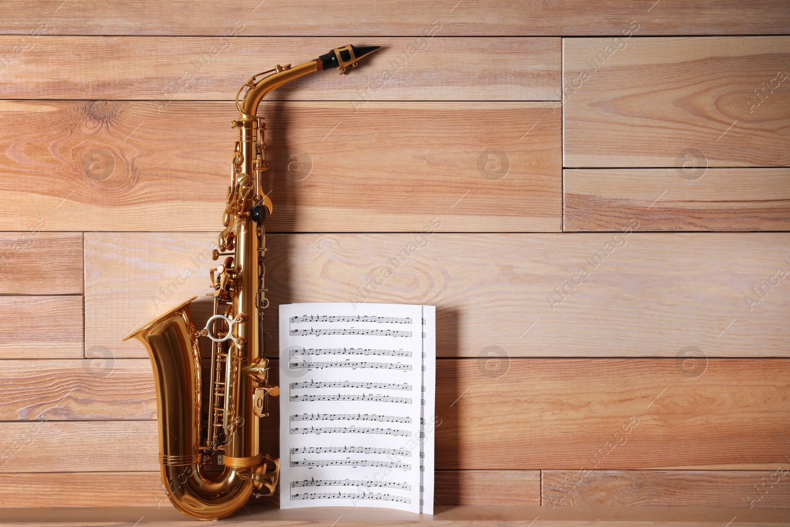 Photo of Beautiful saxophone and note sheets on table near wooden wall, space for text