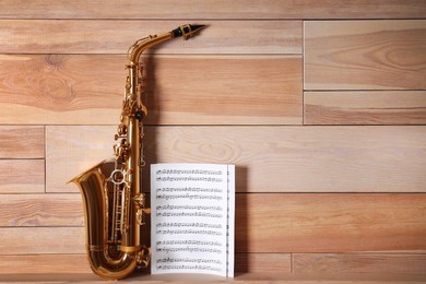 Photo of Beautiful saxophone and note sheets on table near wooden wall, space for text