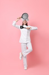 Photo of Professional chef with frying pan and spatula having fun on pink background