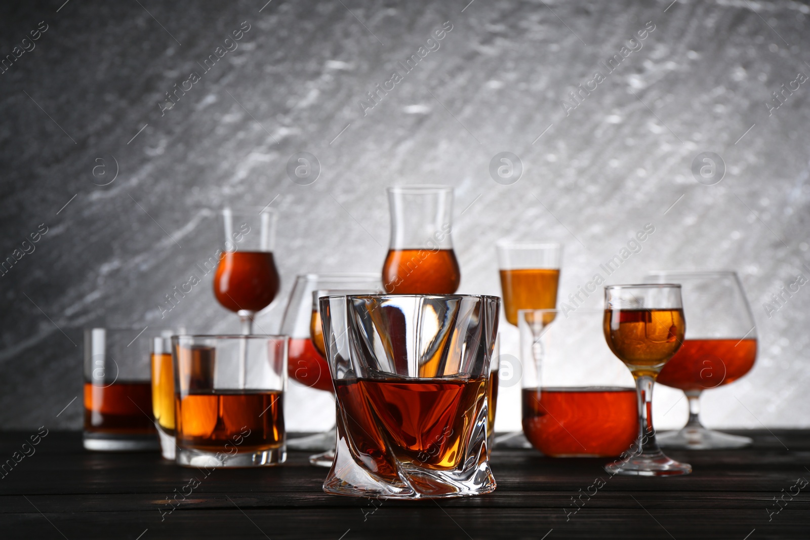 Photo of Different delicious liqueurs in glasses on dark wooden table