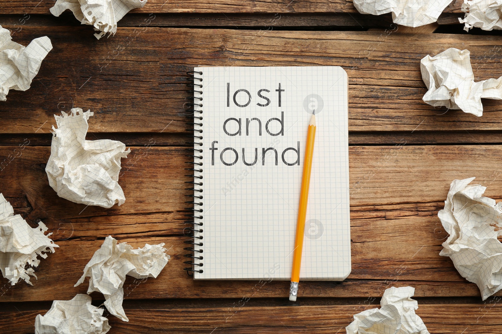 Image of Notebook with phrase Lost and Found, pencil, crumpled sheets of paper on wooden background, flat lay