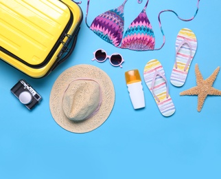 Photo of Yellow suitcase and beach objects on blue background, flat lay