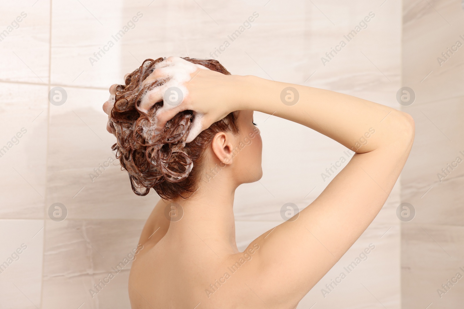 Photo of Young woman washing her hair with shampoo in shower, back view