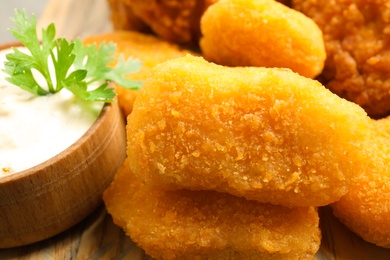 Tasty fried chicken nuggets with sauce on serving board, closeup