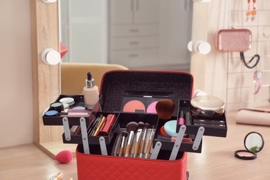 Beautician case with professional makeup products and tools on wooden dressing table