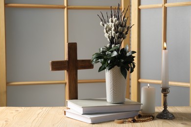 Photo of Cross, burning candles, books, rosary beads and bouquet with willow branches on wooden table