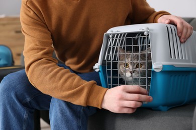 Photo of Travel with pet. Man closing carrier with cat on sofa indoors, closeup