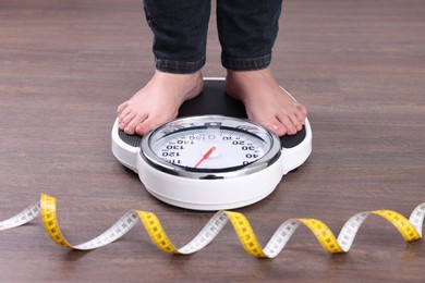 Photo of Woman using scales on floor near measuring tape, closeup. Overweight problem