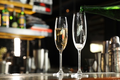 Pouring champagne from bottle into glass on counter in bar. Space for text