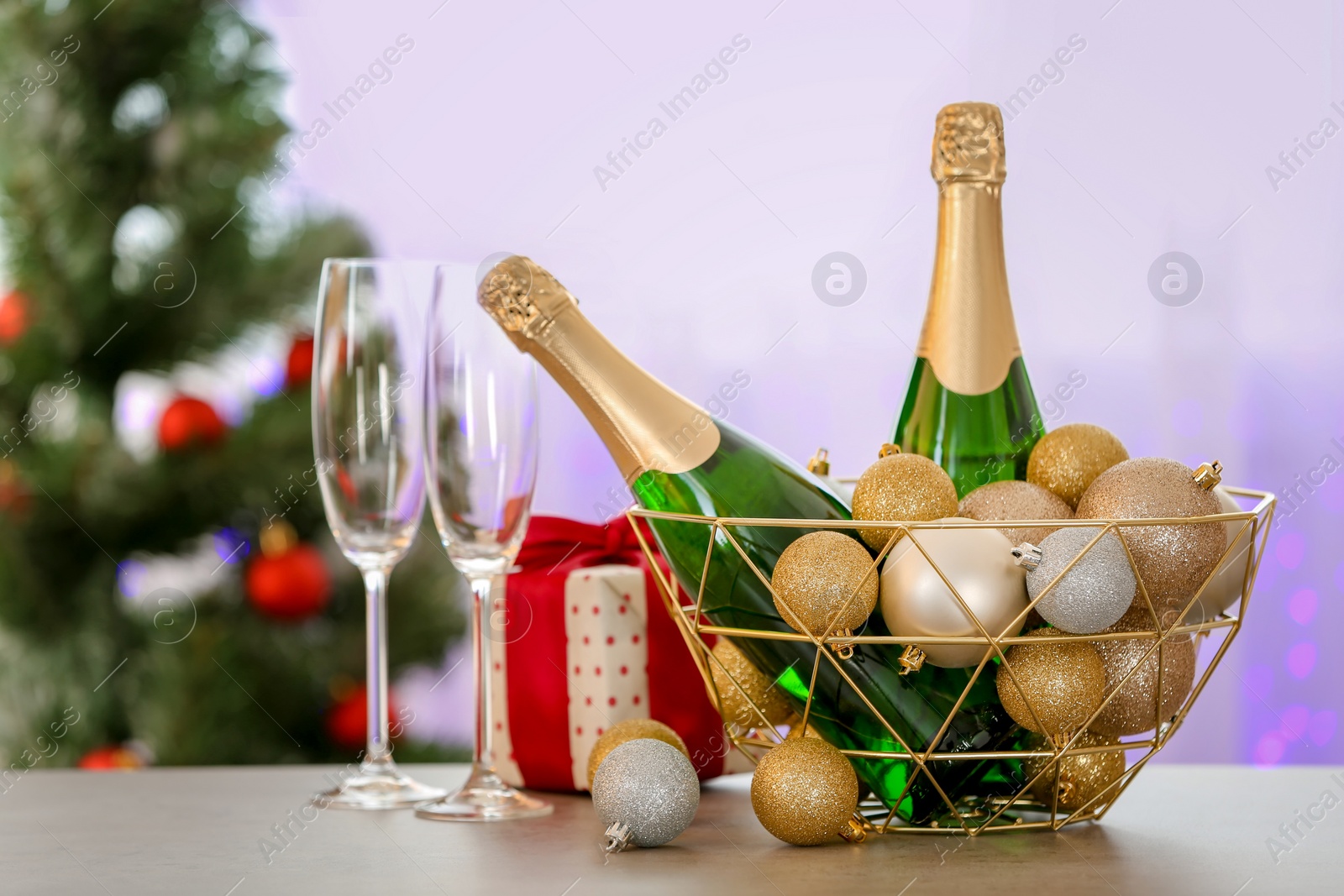 Photo of New year composition with bottles of champagne in decorative basket and blurred Christmas tree on background