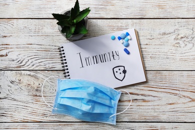 Photo of Notebook with word Immunity and medical supplies on white wooden table, flat lay