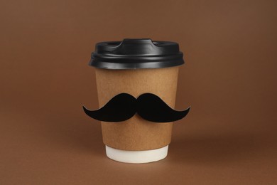 Photo of Paper cup of drink with fake mustache on brown background