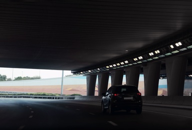 Modern car driving through illuminated highway tunnel