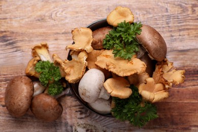 Bowl with different mushrooms and parsley on wooden table, flat lay