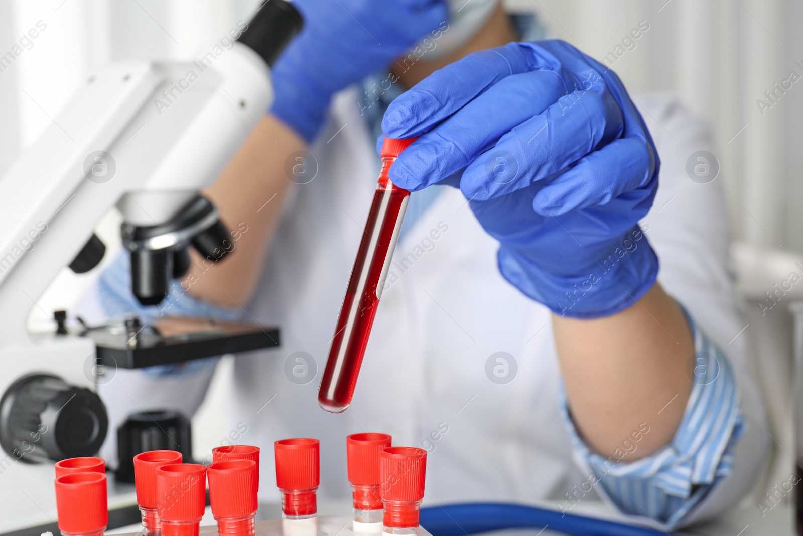 Photo of Scientist holding test tube with blood sample at table, closeup. Virus research