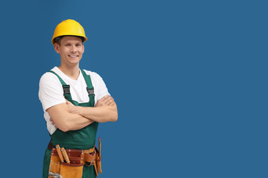 Photo of Handsome carpenter with tool belt on blue background. Space for text