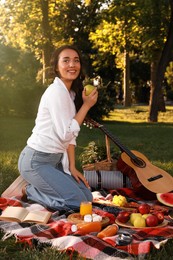 Photo of Happy young woman having picnic on plaid in summer park