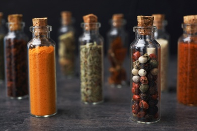 Photo of Glass bottles with different spices on table against dark background, closeup