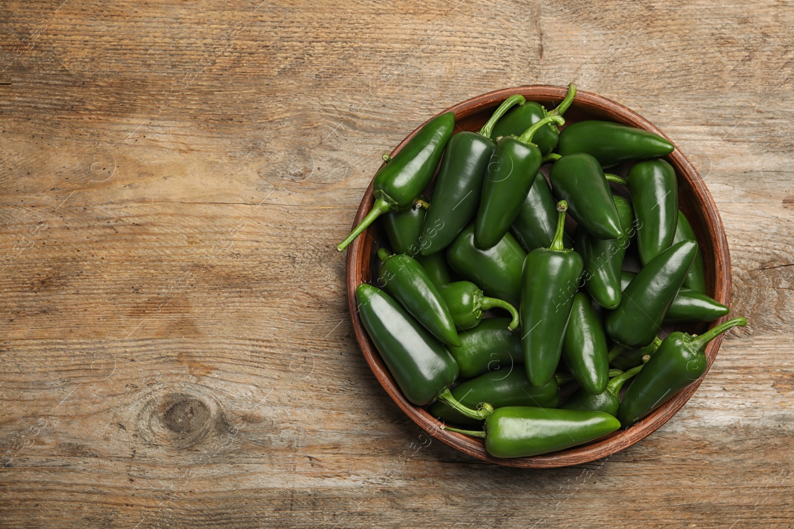 Photo of Bowl with green hot chili peppers on wooden table, top view. Space for text