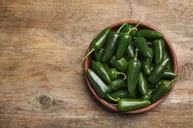 Photo of Bowl with green hot chili peppers on wooden table, top view. Space for text