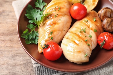 Plate with fried chicken breasts and garnish on wooden table, closeup