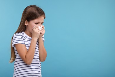 Sick girl with tissue coughing on light blue background, space for text