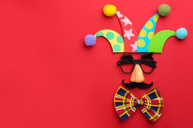 Photo of Flat lay composition with clown's face made of party glasses, hat and bow tie on red background. Space for text