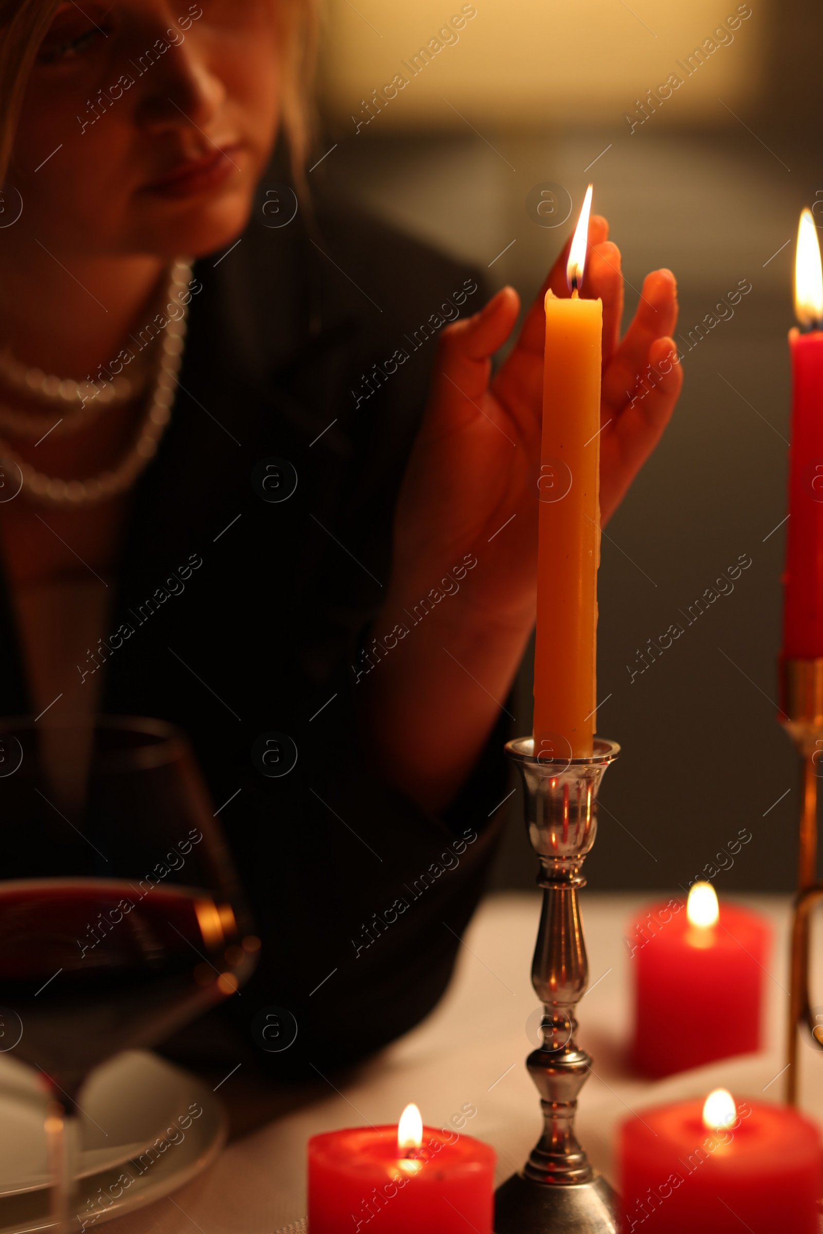 Photo of Beautiful young woman near burning candle at table in restaurant, closeup
