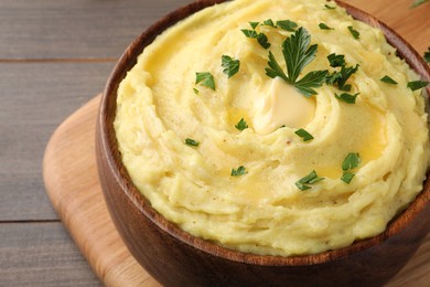 Photo of Bowl of freshly cooked mashed potatoes with parsley served on wooden table, closeup