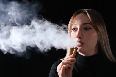 Young woman using electronic cigarette on black background