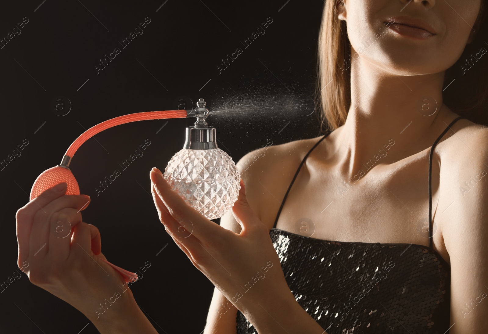 Photo of Young woman applying perfume on neck against black background, closeup