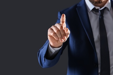 Photo of Businessman touching empty virtual screen against dark background, focus on hand