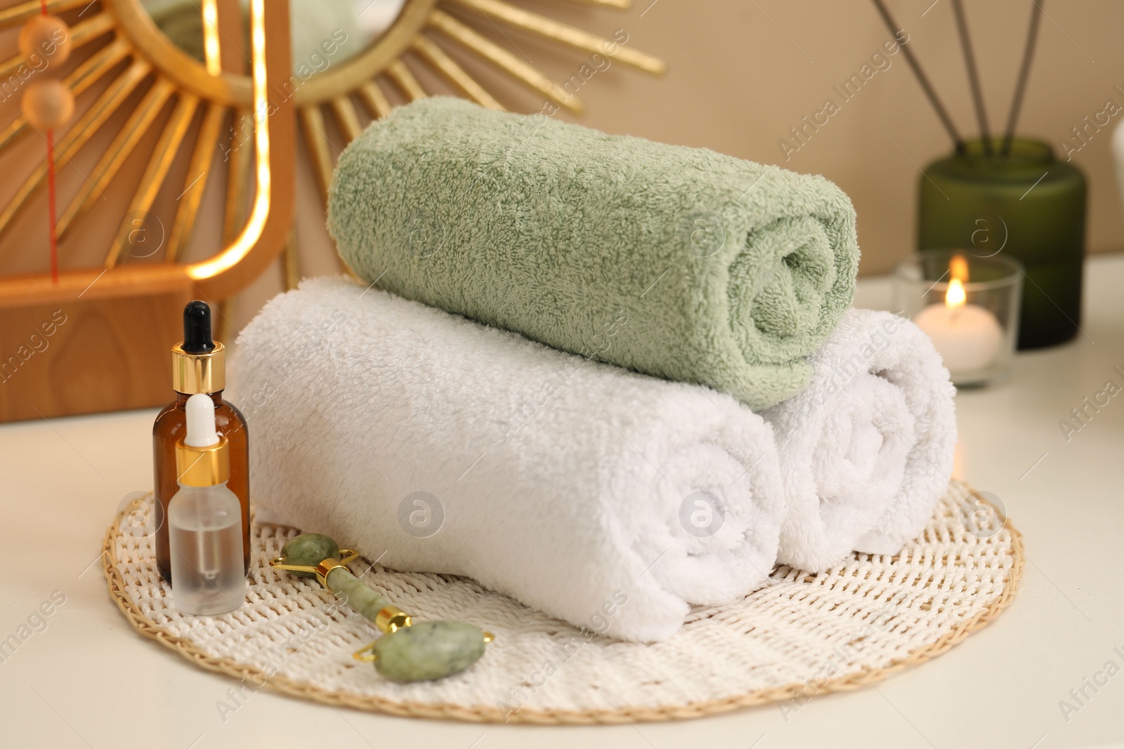 Photo of Spa composition. Rolled towels, cosmetic products and face roller on table