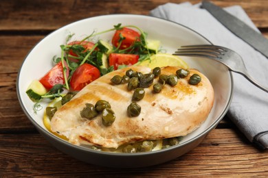 Photo of Delicious cooked chicken fillet with capers and salad served on wooden table, closeup