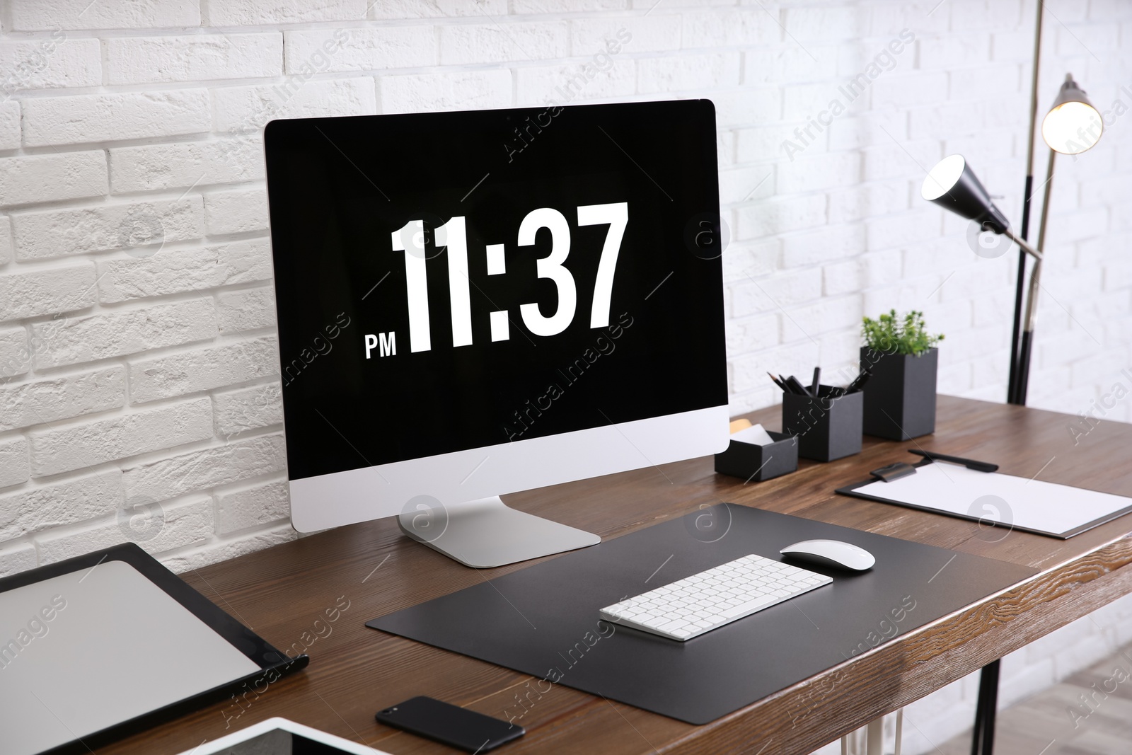 Photo of Modern workplace interior with computer and devices on table near brick wall