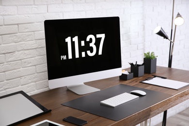 Modern workplace interior with computer and devices on table near brick wall