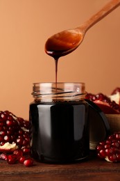 Photo of Spoon with tasty pomegranate sauce over glass jar at wooden table