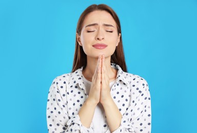 Woman with clasped hands praying on turquoise background