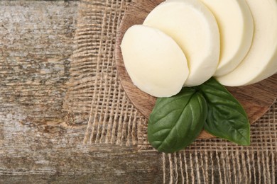 Photo of Board with tasty mozzarella slices and basil leaves on wooden table, above view. Space for text