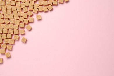 Brown sugar cubes on pink background, flat lay. Space for text