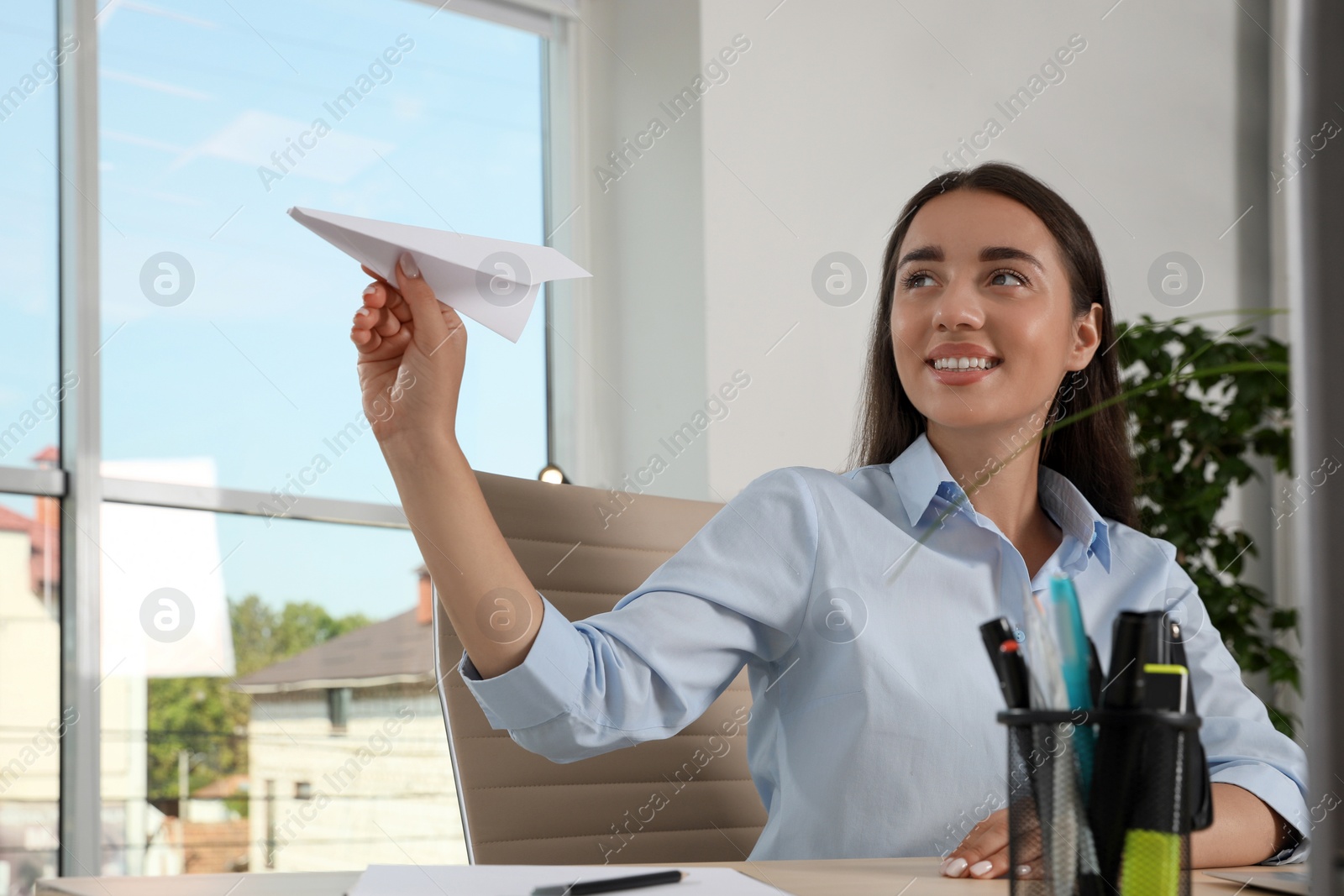 Photo of Beautiful young woman playing with paper plane at desk in office