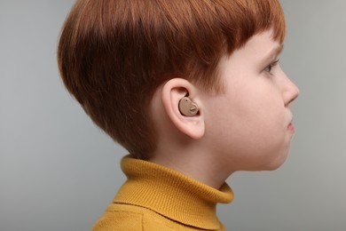 Photo of Little boy with hearing aid on grey background, closeup