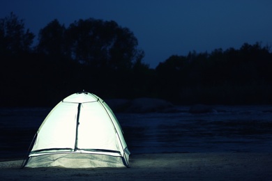 Photo of Small camping tent glowing in twilight outdoors. Space for text