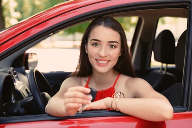 Beautiful young woman with key sitting in car