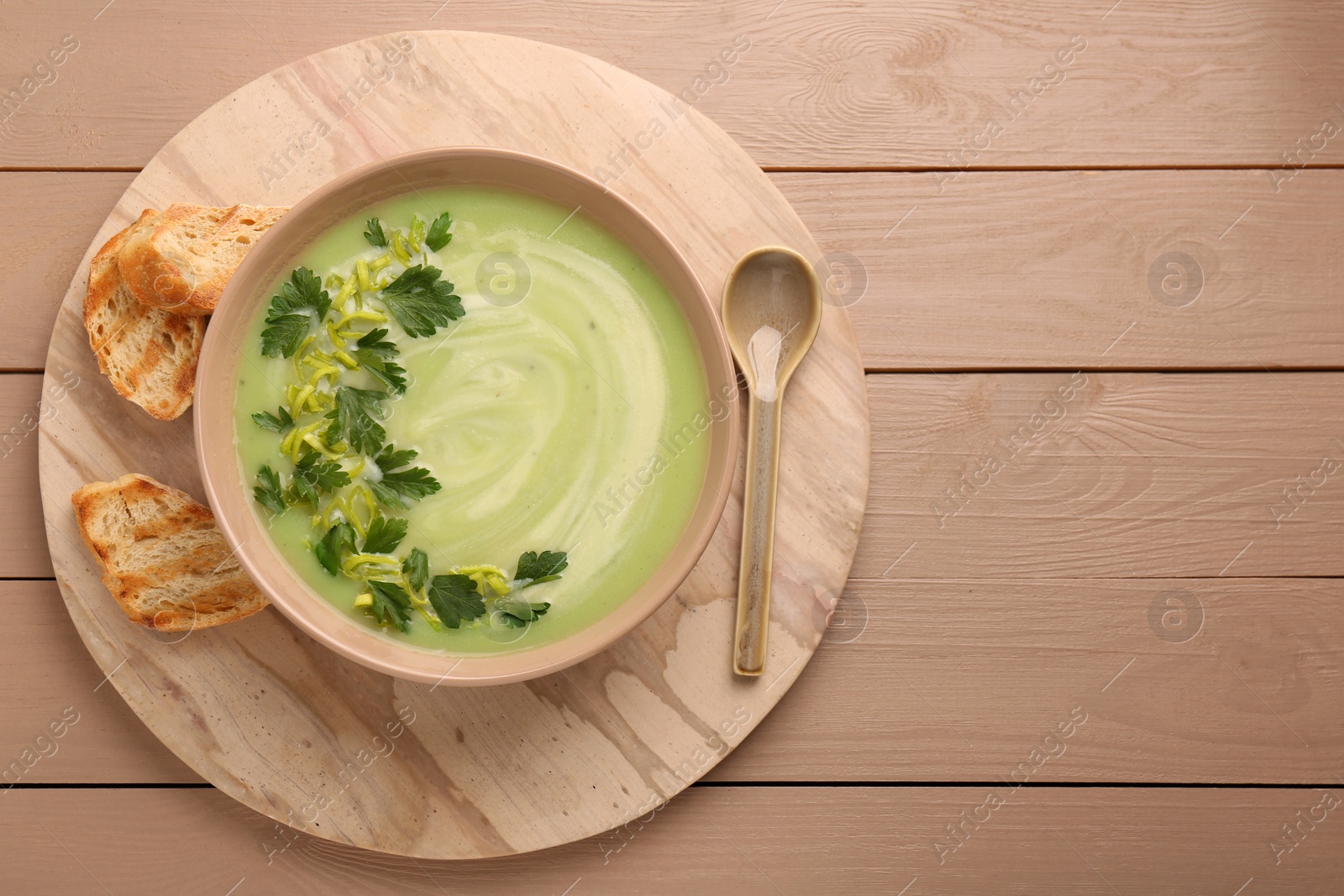 Photo of Delicious leek soup served on beige wooden table, top view. Space for text