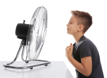 Little boy enjoying air flow from fan on white background. Summer heat