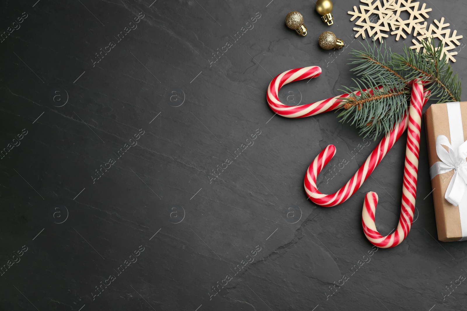 Photo of Flat lay composition with candy canes and Christmas decor on black table. Space for text