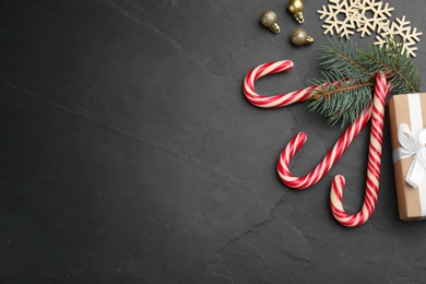 Flat lay composition with candy canes and Christmas decor on black table. Space for text
