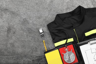 Referee jersey, whistle and other equipment on grey table, top view. Space for text